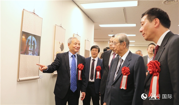 “湖州印象”攝影展主創(chuàng)、世界華人攝影協(xié)會副會長馮學(xué)敏向吳江浩大使、福田康夫前首相等嘉賓介紹展出作品。（人民網(wǎng) 許可攝）