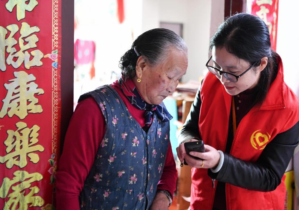在福州市長(zhǎng)樂(lè)區(qū)航城街道籌岐村，智慧養(yǎng)老平臺(tái)派駐社區(qū)的助老員（右）在為老人陳鳳英（左）講解養(yǎng)老定制手機(jī)的用法（2021年11月26日攝）。新華社記者 魏培全 攝