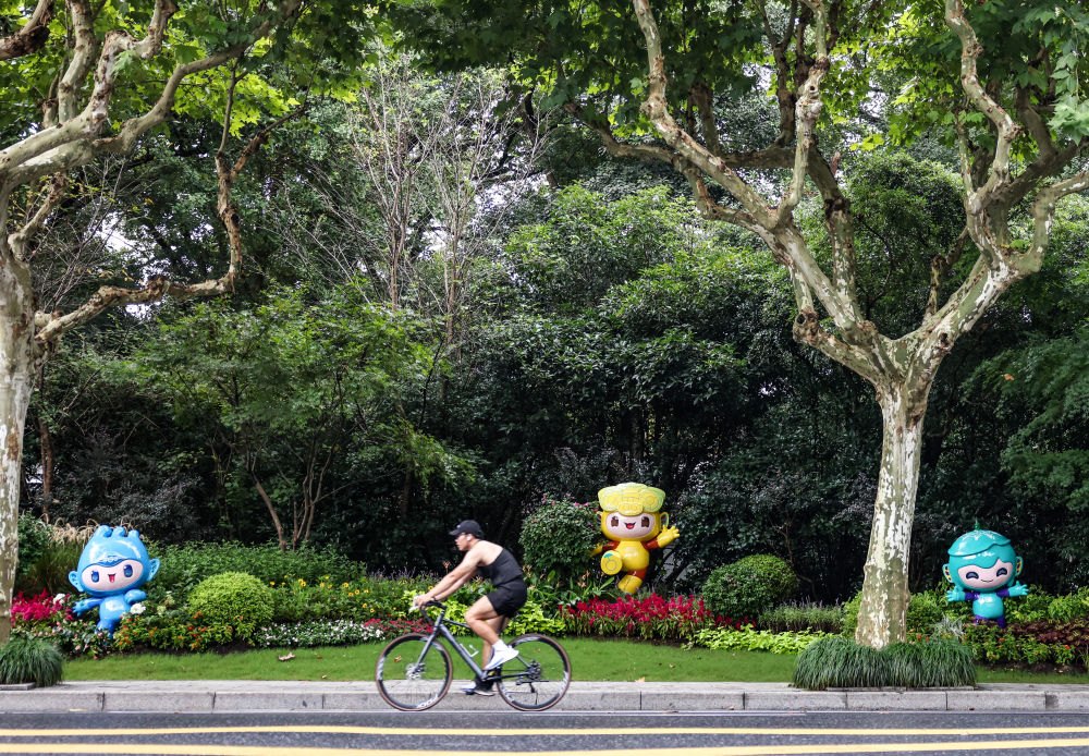 市民在杭州市南山路上一處亞運會主題吉祥物雕塑前騎自行車。