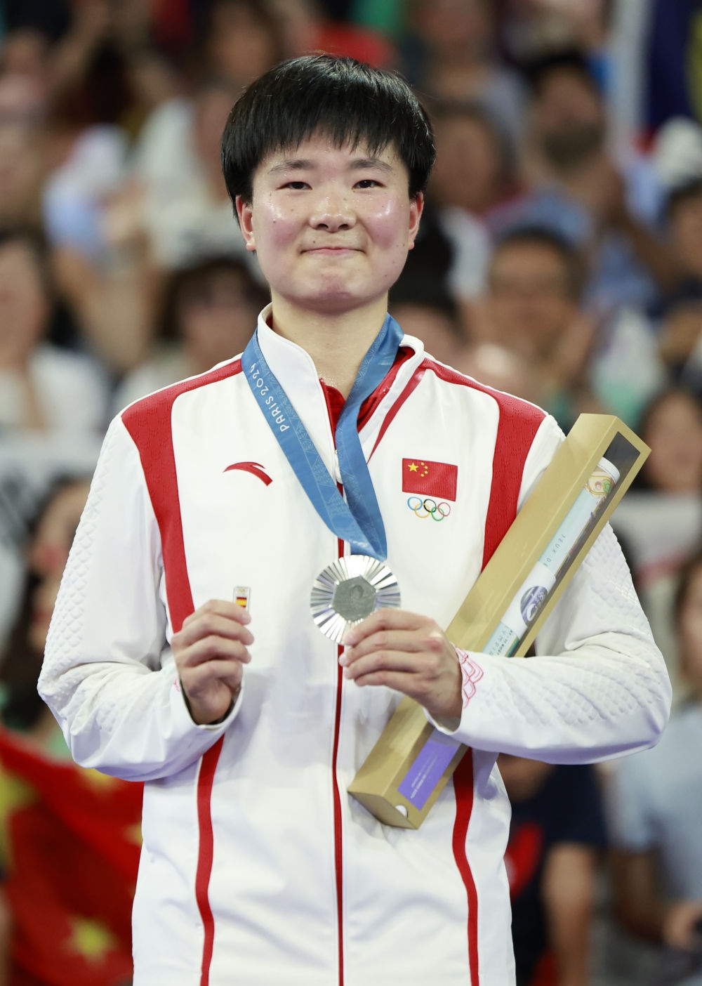 巴黎奧運(yùn)會(huì)羽毛球女子單打亞軍、中國(guó)選手何冰嬌在頒獎(jiǎng)儀式上一手握著銀牌，一手握著西班牙奧委會(huì)徽章（2024年8月5日攝）。新華社記者 任正來(lái) 攝