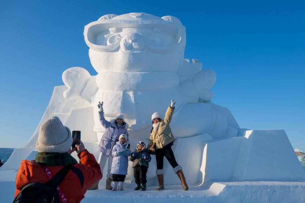 2025年1月3日，在黑龍江哈爾濱冰雪大世界園區(qū)，游客與亞冬會吉祥物雪雕“濱濱”合影